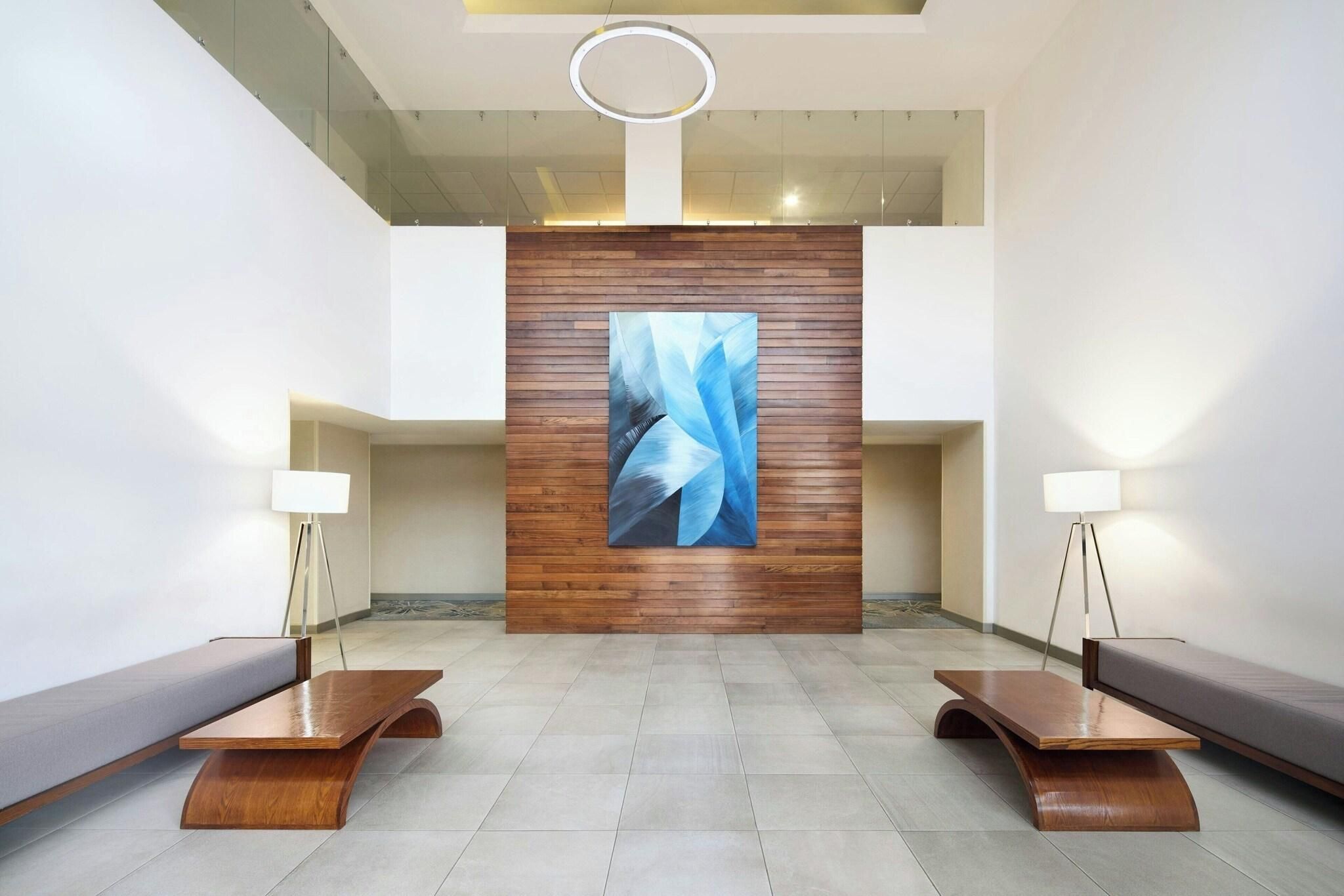 Un vestíbulo moderno con un panel de madera central, dos mesas auxiliares y un cuadro abstracto grande.