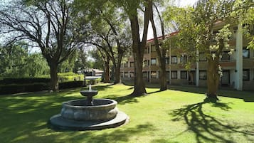Ein Innenhof mit einem Brunnen, Bäumen und einem Gebäude mit vielen Fenstern.