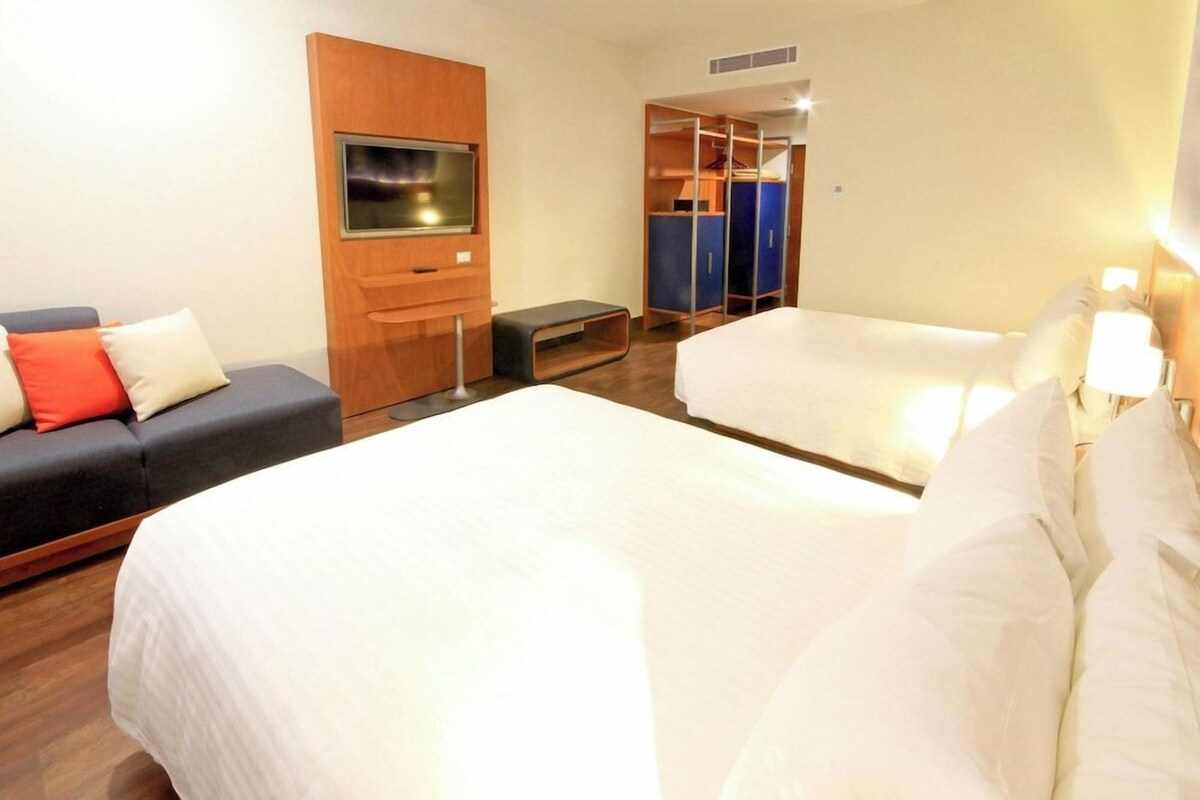 Une chambre d’hôtel avec deux lits, un canapé, une télévision et une armoire.