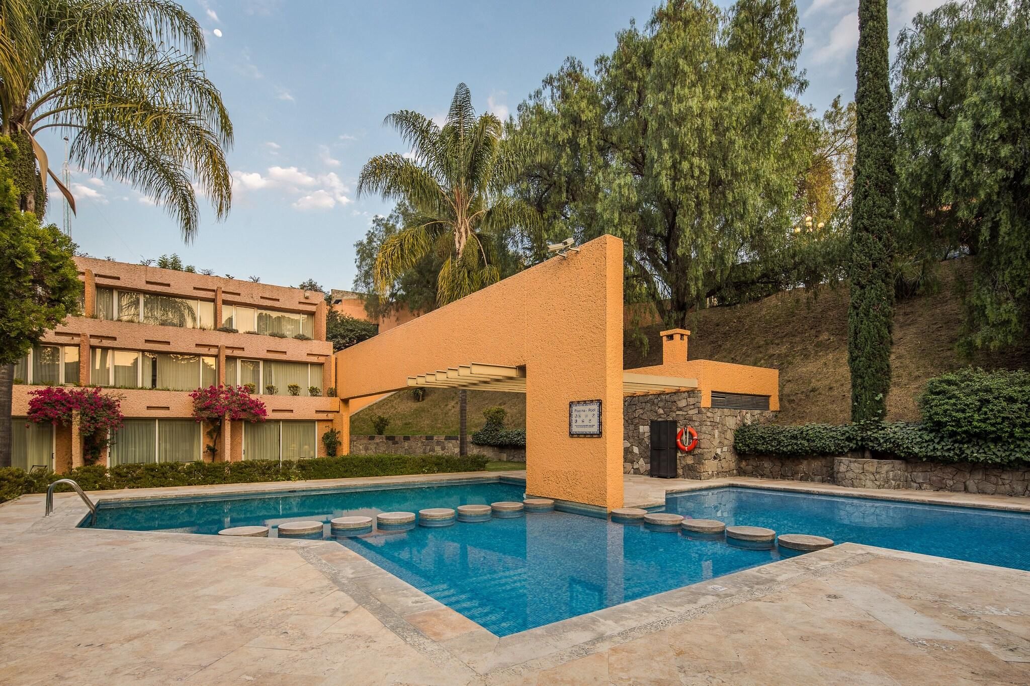 Zona de piscina con vista despejada, escalones que bajan al agua y un edificio de fachada de ladrillo al fondo.