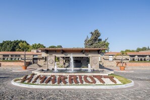 L'ingresso di un hotel con una fontana, un cartello con la scritta 'MARRIOTT' e un'area verde con alberi e arbusti.