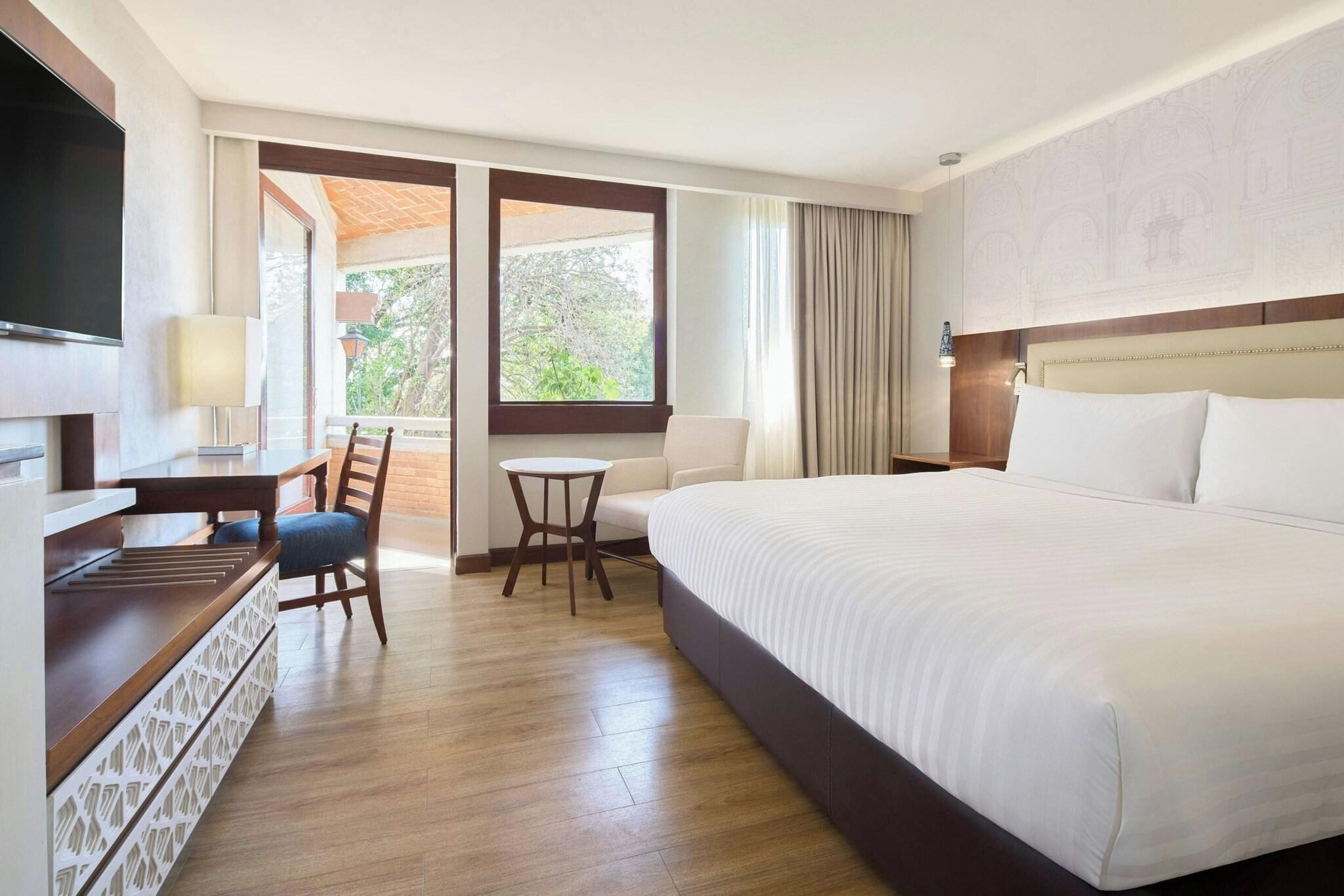 Habitación de hotel con cama, escritorio, silla, televisor y ventana con vistas.