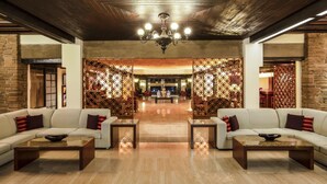 Een ruime hal met een hoge plafond, een kroonluchter en een centraal zithoek met banken en salontafels.