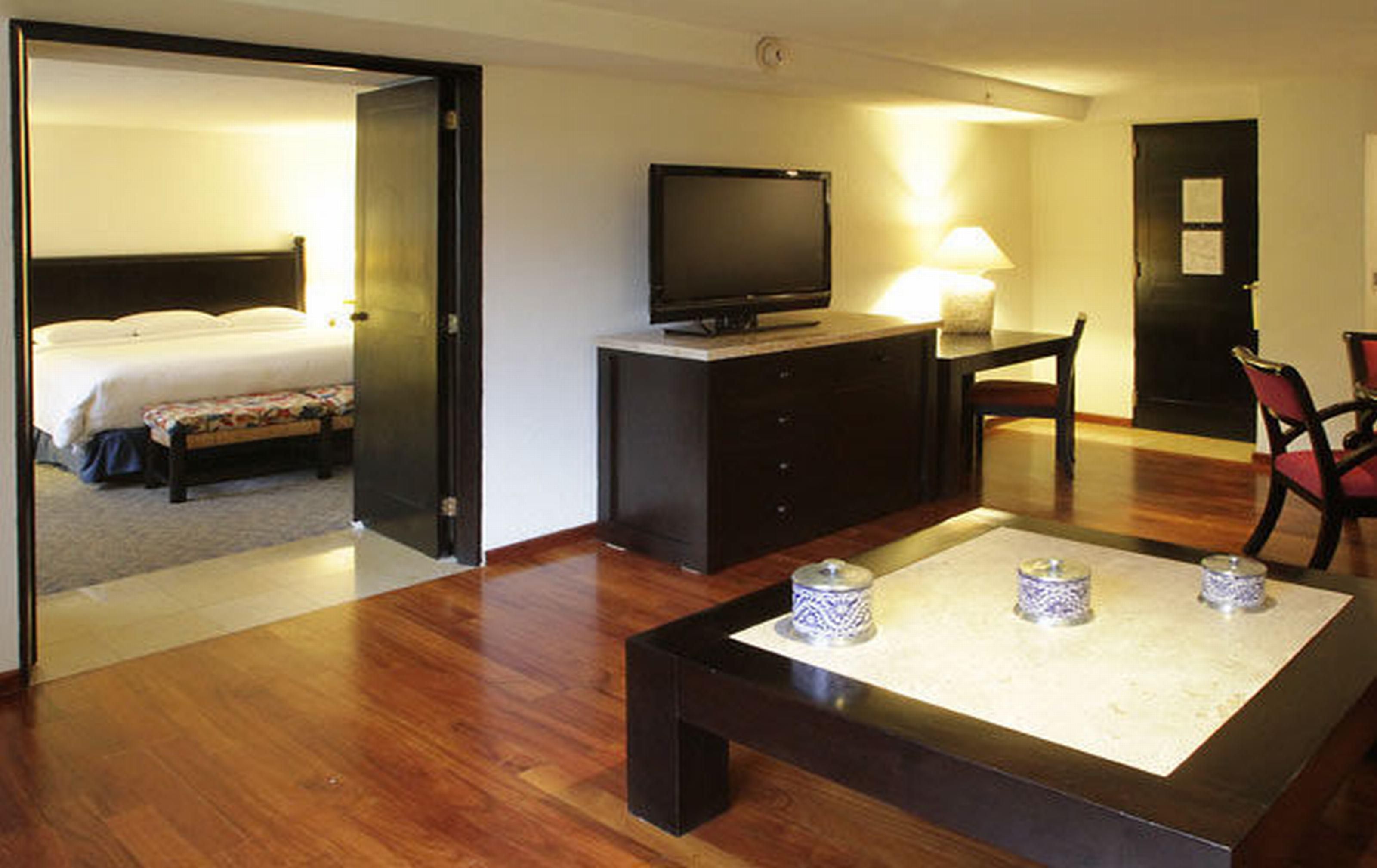 Ein Hotelzimmer mit einem Bett, einem Fernseher auf einem Tisch, einem Schreibtisch mit einer Lampe und einem Sessel.