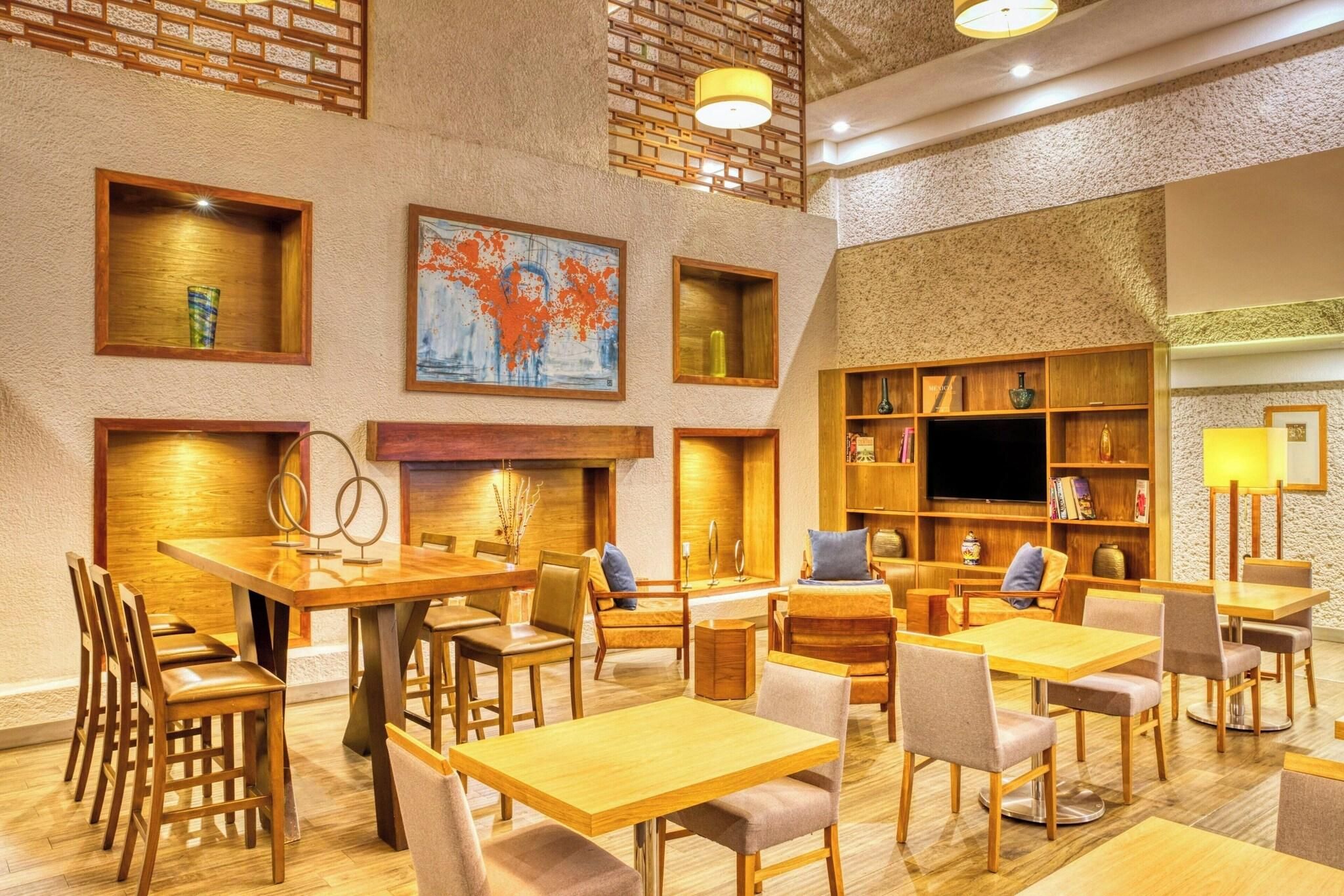 A hotel lobby with wooden furniture, a fireplace, a television, and artwork on the walls.