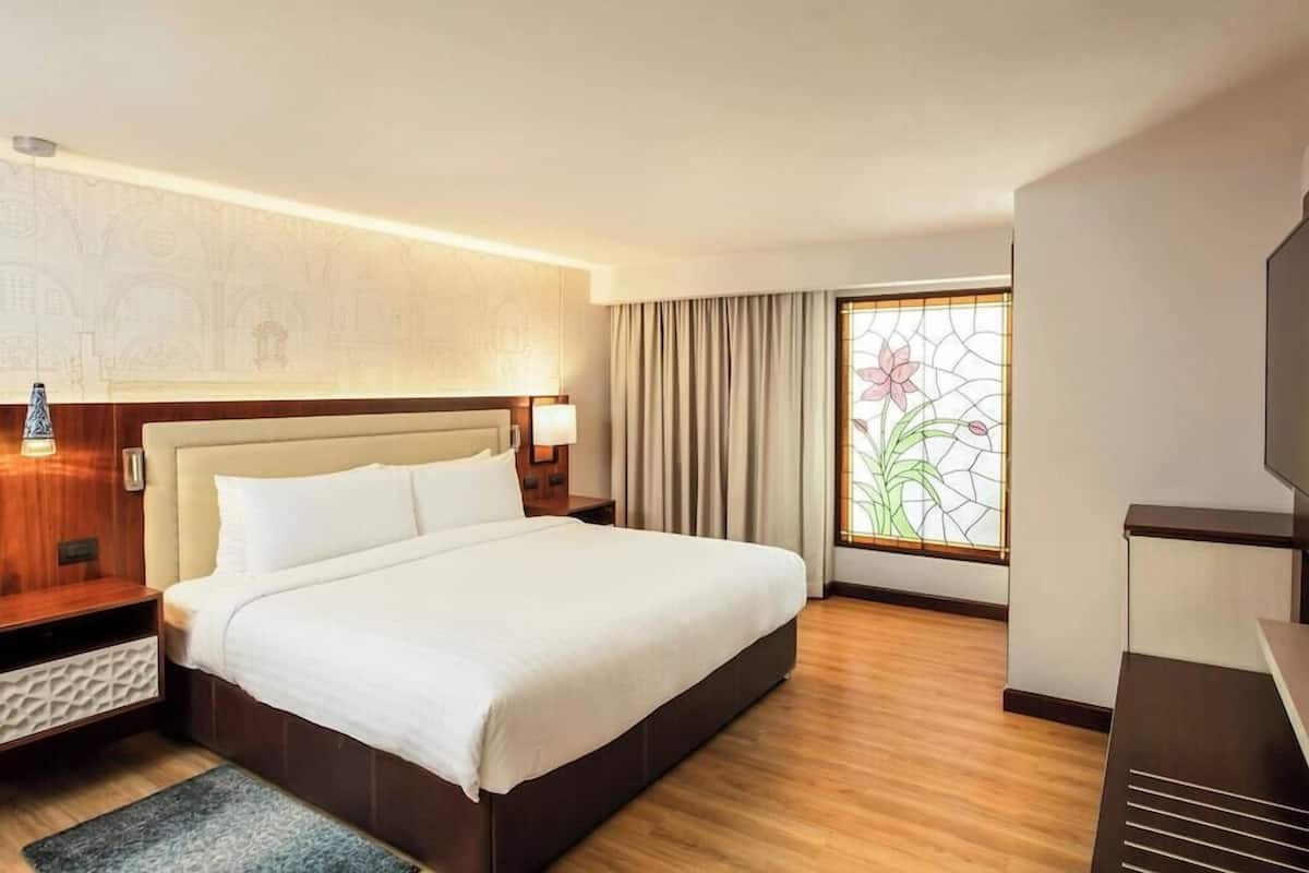 Ein Hotelzimmer mit einem großen Bett, einem Nachttisch, einer Lampe, einem Fernseher und einem Fenster mit Vorhängen.