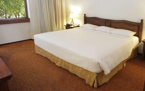 A hotel room with a large bed, a nightstand with a lamp, and a window with curtains. - Marriott Puebla Hotel Meson del Angel (Puebla)