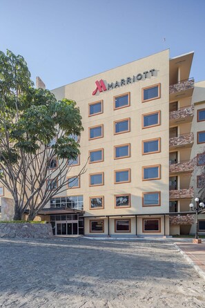 A multi-story hotel with a prominent Marriott logo, a stone facade, and a landscaped entrance area.