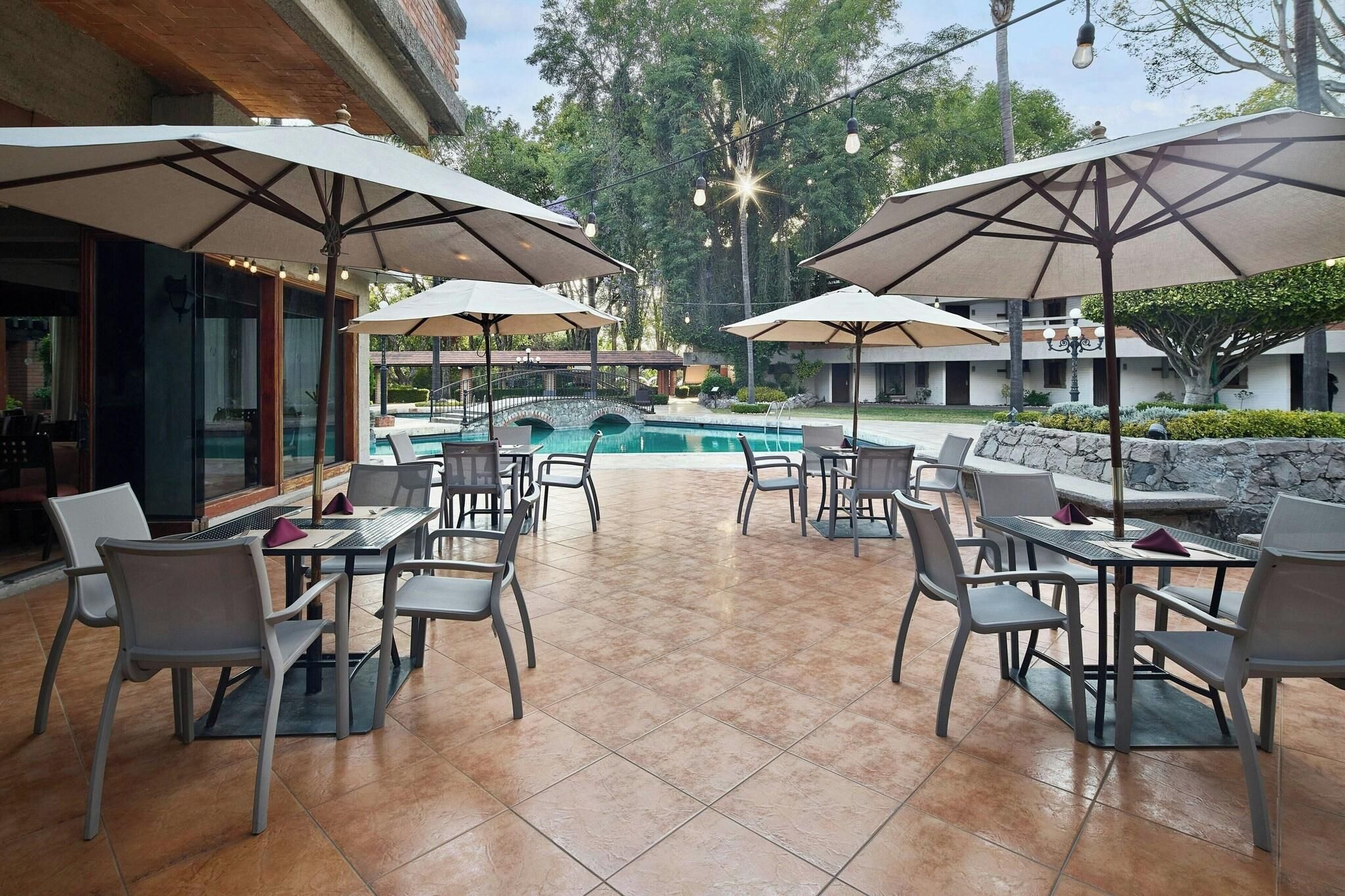An outdoor patio area with tables and chairs, umbrellas, and a swimming pool.