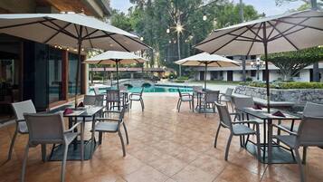 An outdoor patio area with tables and chairs, umbrellas, and a swimming pool.