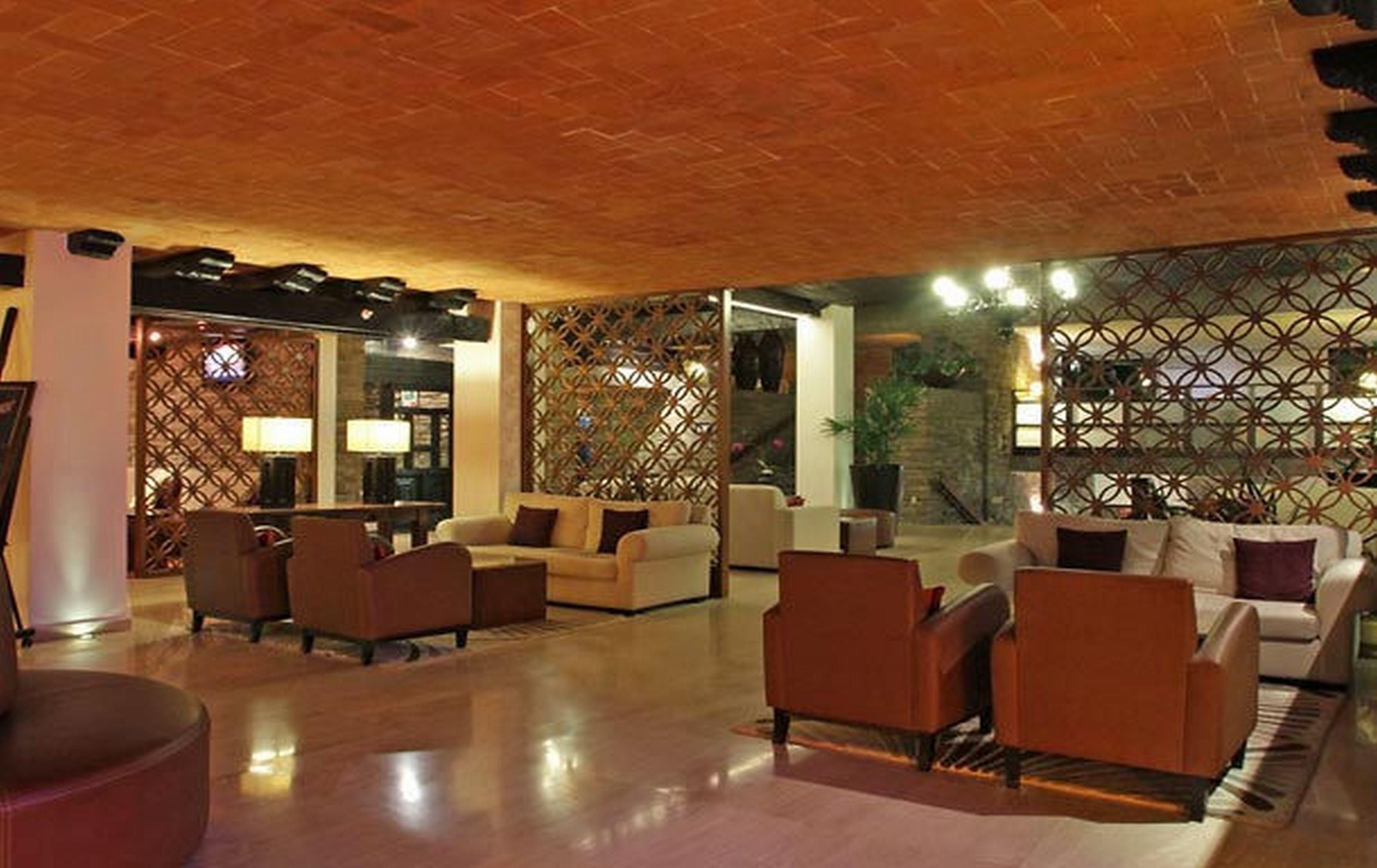 Un'ampia hall con soffitto alto, zona relax con divani e poltrone, e pannelli decorativi a traliccio.
