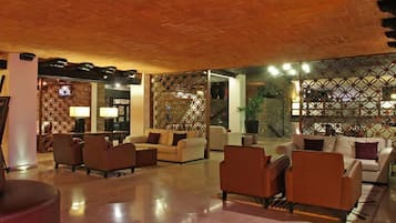 Un'ampia hall con soffitto alto, zona relax con divani e poltrone, e pannelli decorativi a traliccio.