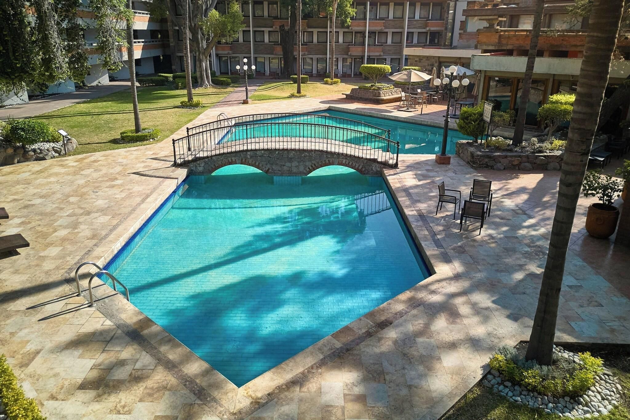 Una piscina con bordo in pietra, un piccolo ponte e area relax all'aperto.