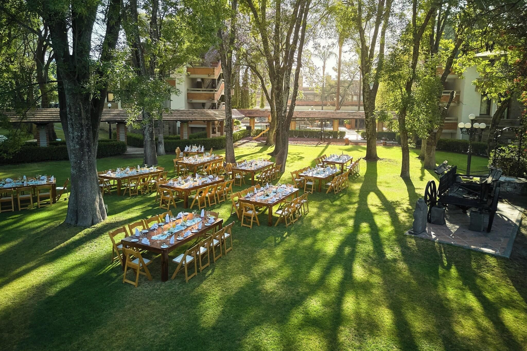 An outdoor dining area with multiple tables and chairs, surrounded by trees and buildings.