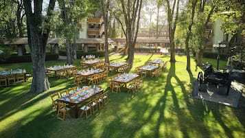 An outdoor dining area with multiple tables and chairs, surrounded by trees and buildings.