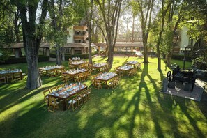 Zona pranzo all'aperto con diversi tavoli e sedie, circondata da alberi ed edifici.