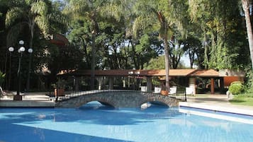 Ein Schwimmbecken mit einer Steinbrücke, umgeben von Bäumen und einem überdachten Pavillon.