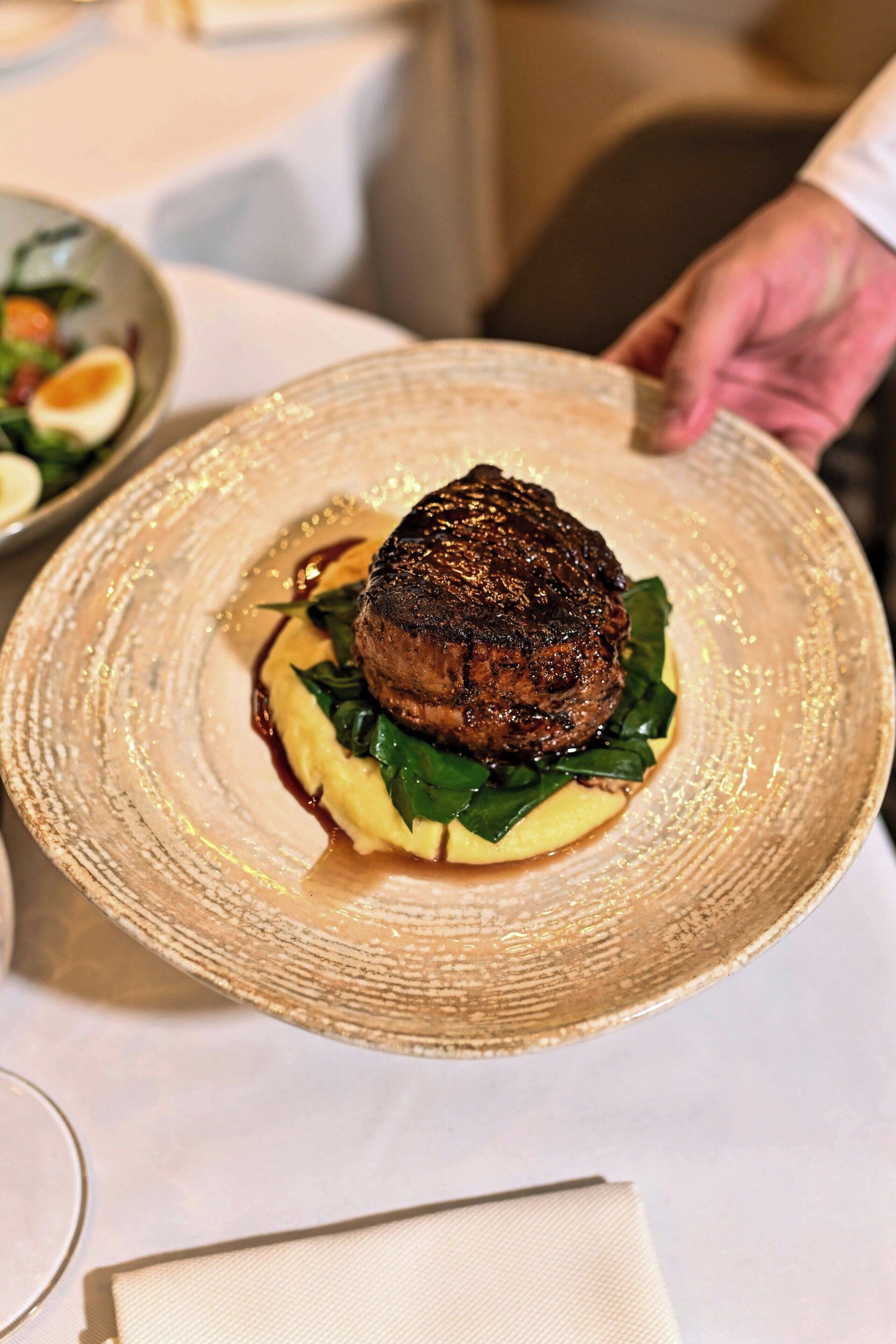 En tallerken med steak, grønt og sauce, holdt af en person.