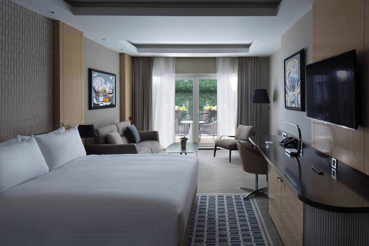 Une chambre d’hôtel moderne dotée d’un grand lit, d’un bureau, d’une télévision et d’un balcon aménagé avec du mobilier d’extérieur.
