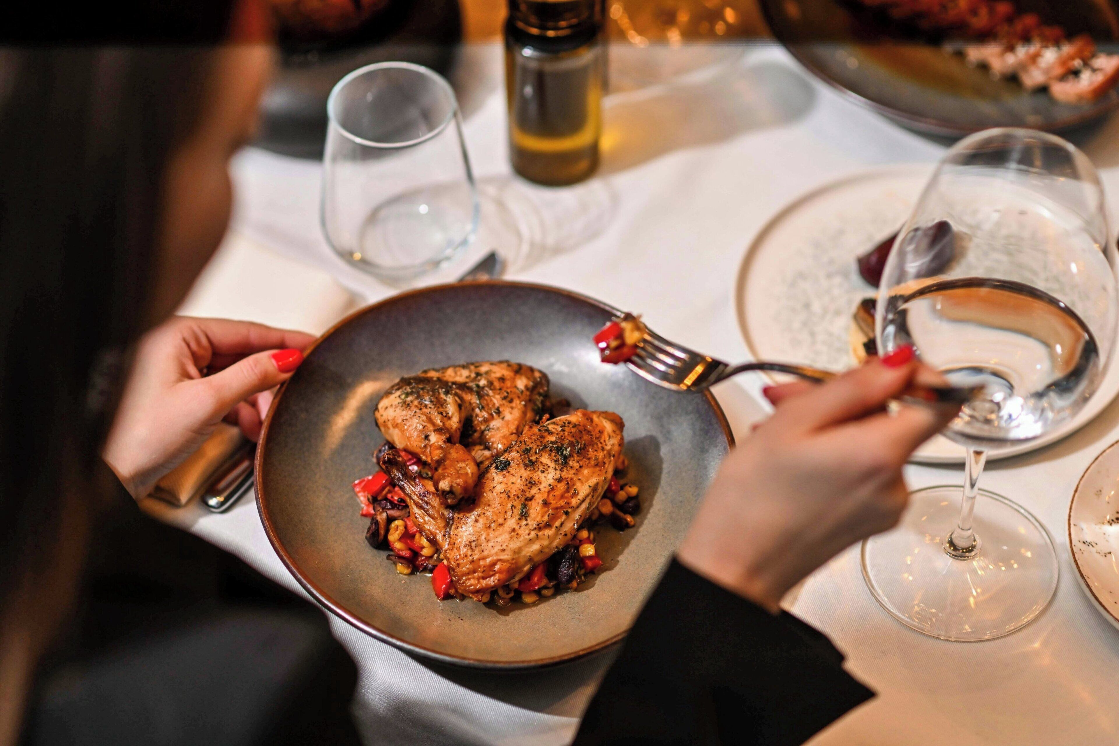 A dining table with a plate of roasted chicken, wine glasses, and a salt and pepper shaker.