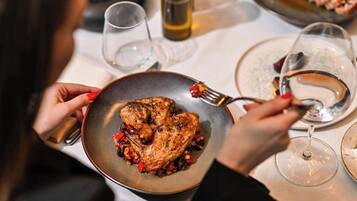 A dining table with a plate of roasted chicken, wine glasses, and a salt and pepper shaker.
