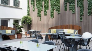 Eine Terrasse im Freien mit Tischen und Stühlen, eine Wand aus Holzlatten und eine grüne Mauer, die mit Efeu bewachsen ist.