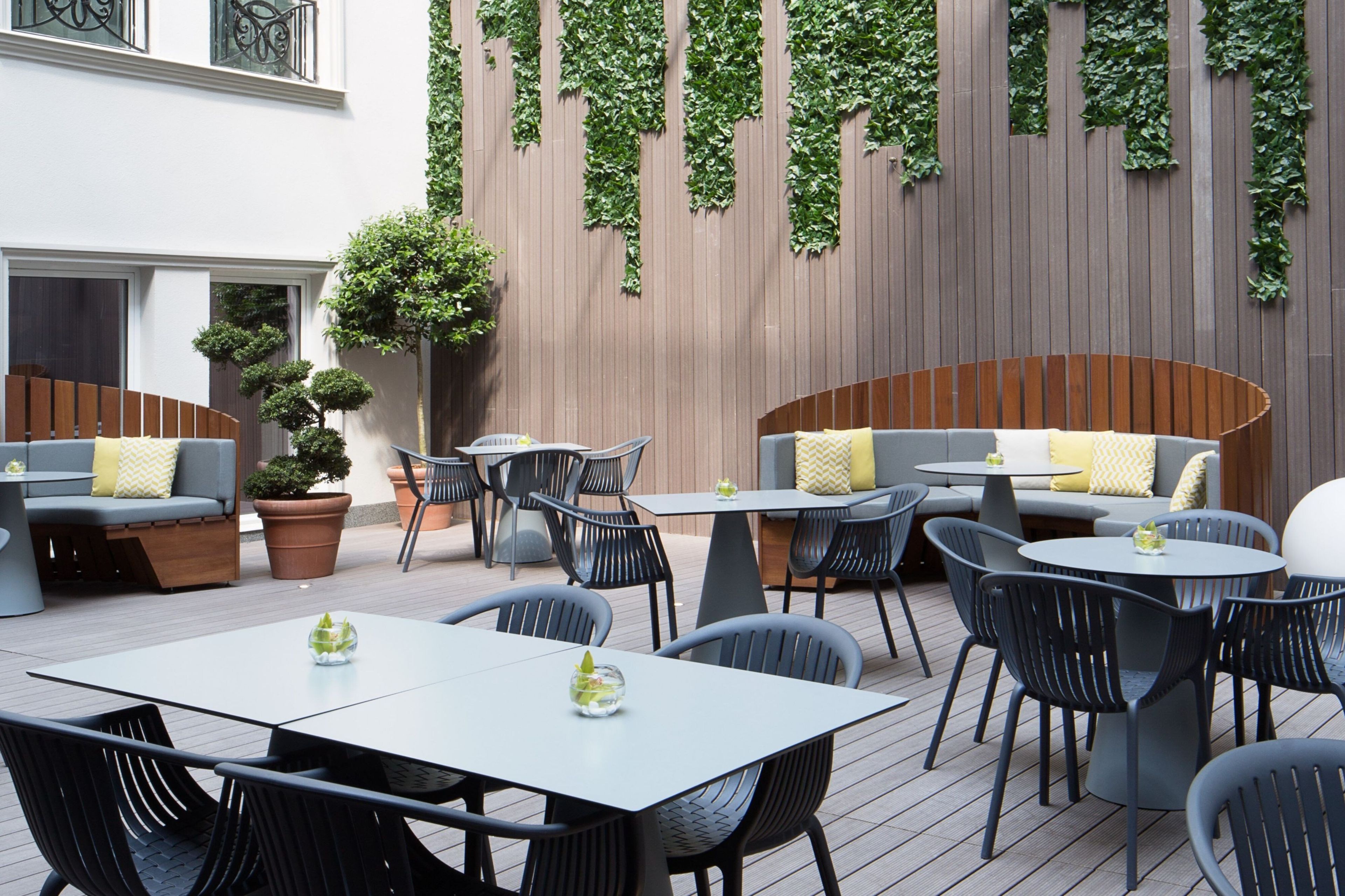 Un espace extérieur aménagé avec des tables et des chaises, un mur en bois agrémenté de plantes grimpantes et un pot de fleurs.