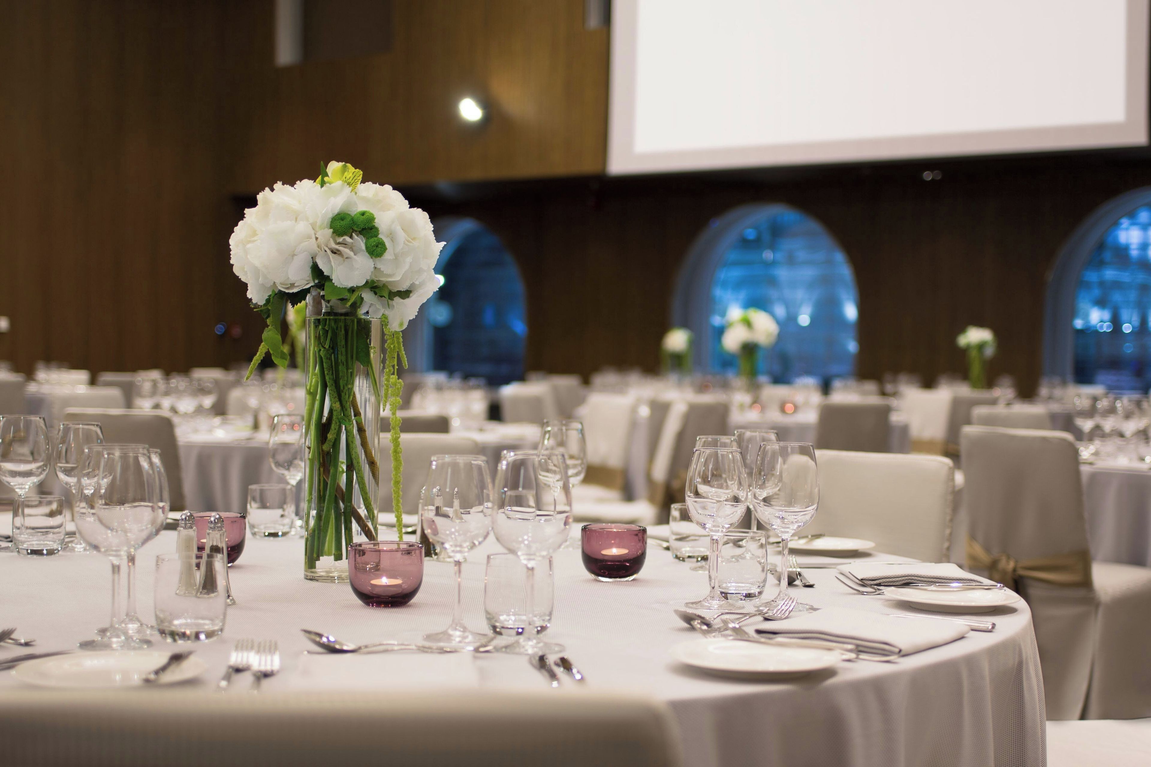 A banquet hall with round tables set for dining, each with cutlery and glasses.