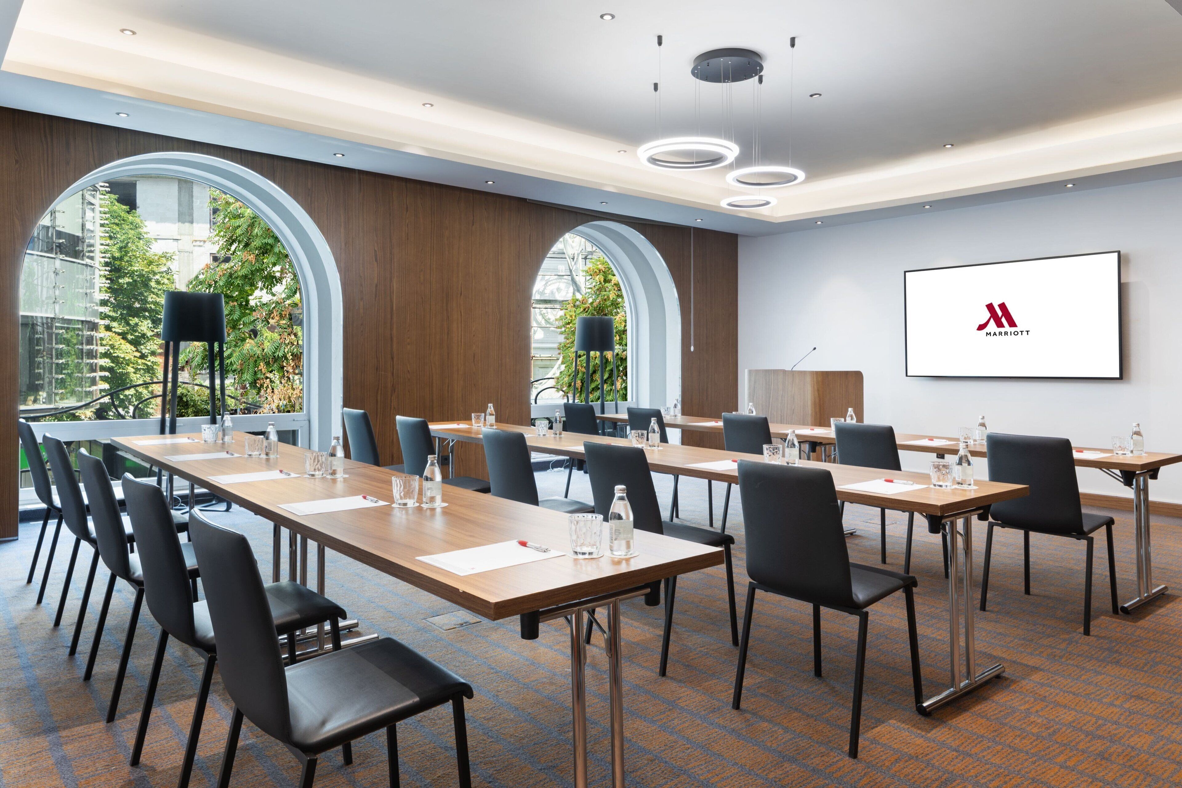 A conference room with long tables, chairs, and a large screen displaying the Marriott logo.
