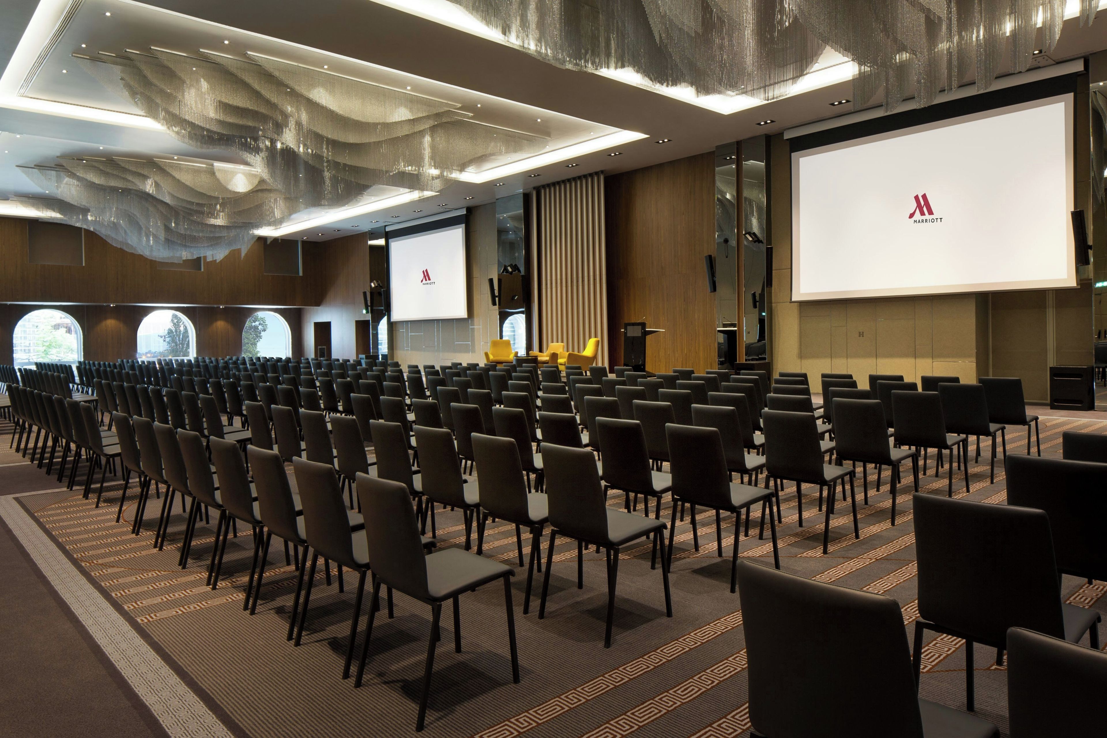 Un salón de conferencias con filas de sillas, una pantalla grande y un atril.