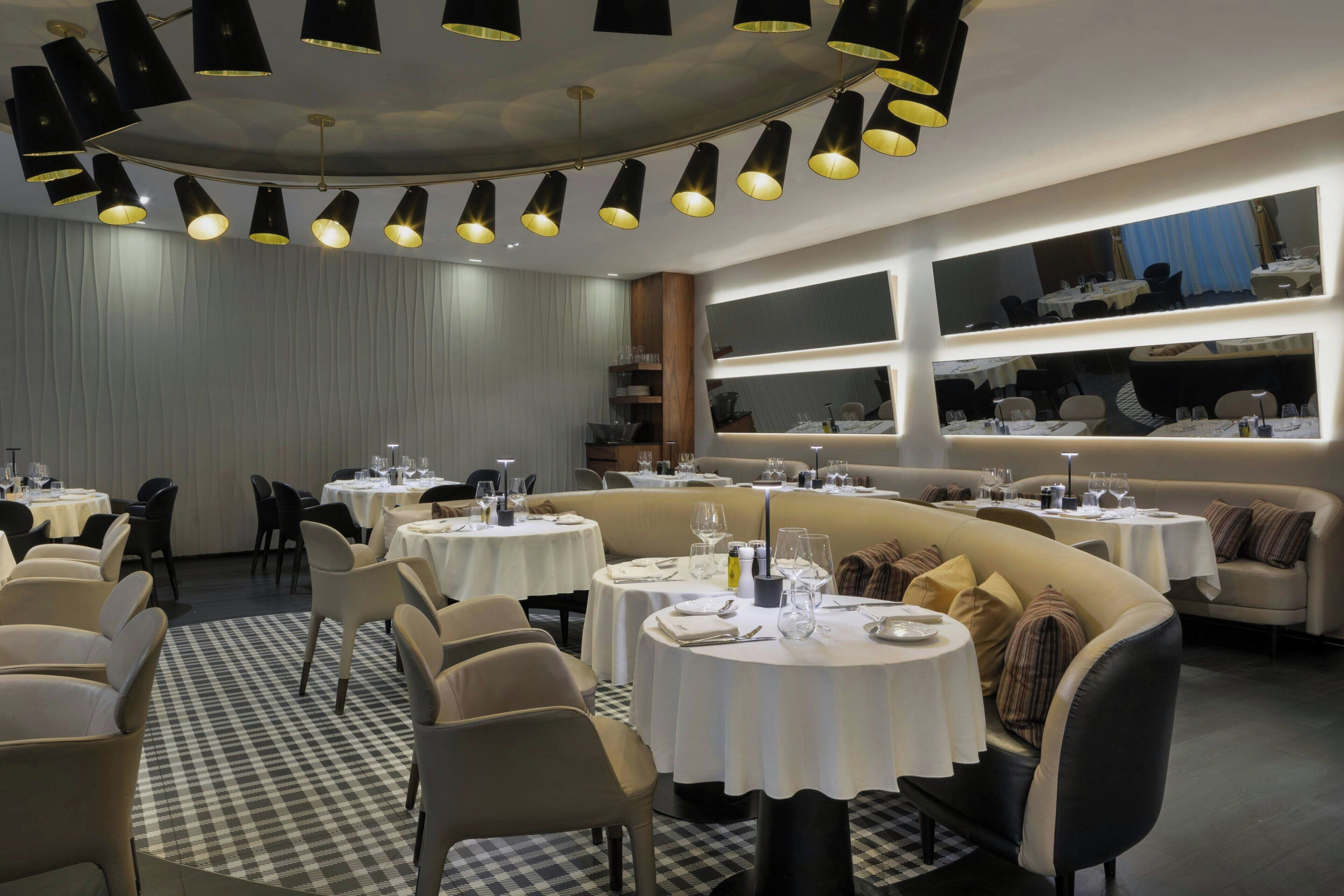 Un restaurante con mesas redondas, sillas negras y suelo a cuadros.