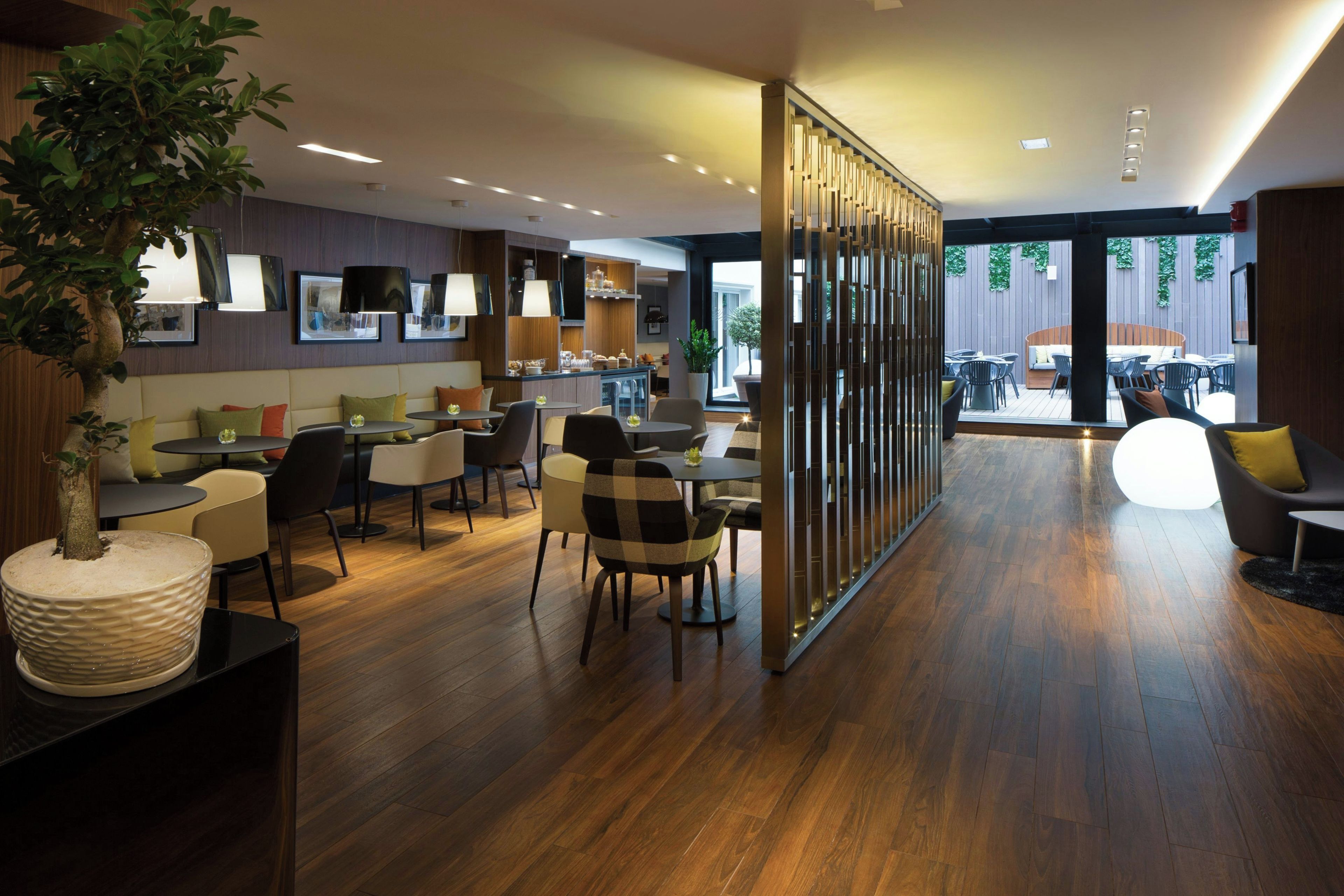 A modern interior with wooden flooring, a bar area, seating arrangements, and a view of the outdoors.