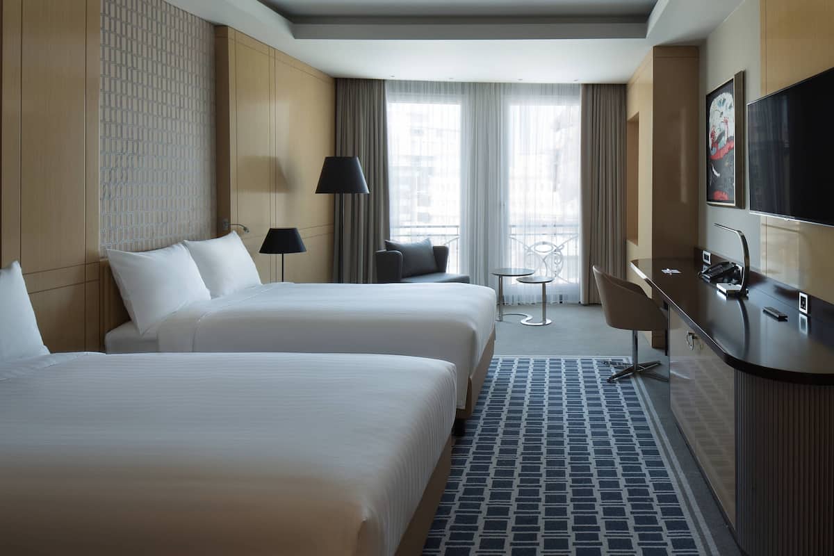 Une chambre d’hôtel avec deux lits, un bureau, une chaise, une télévision et un balcon avec vue.