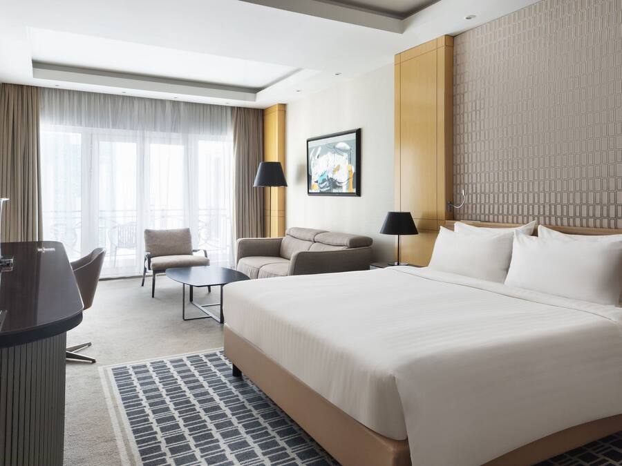 A hotel room with a large bed, a desk, a chair, a sofa, and a window with curtains.