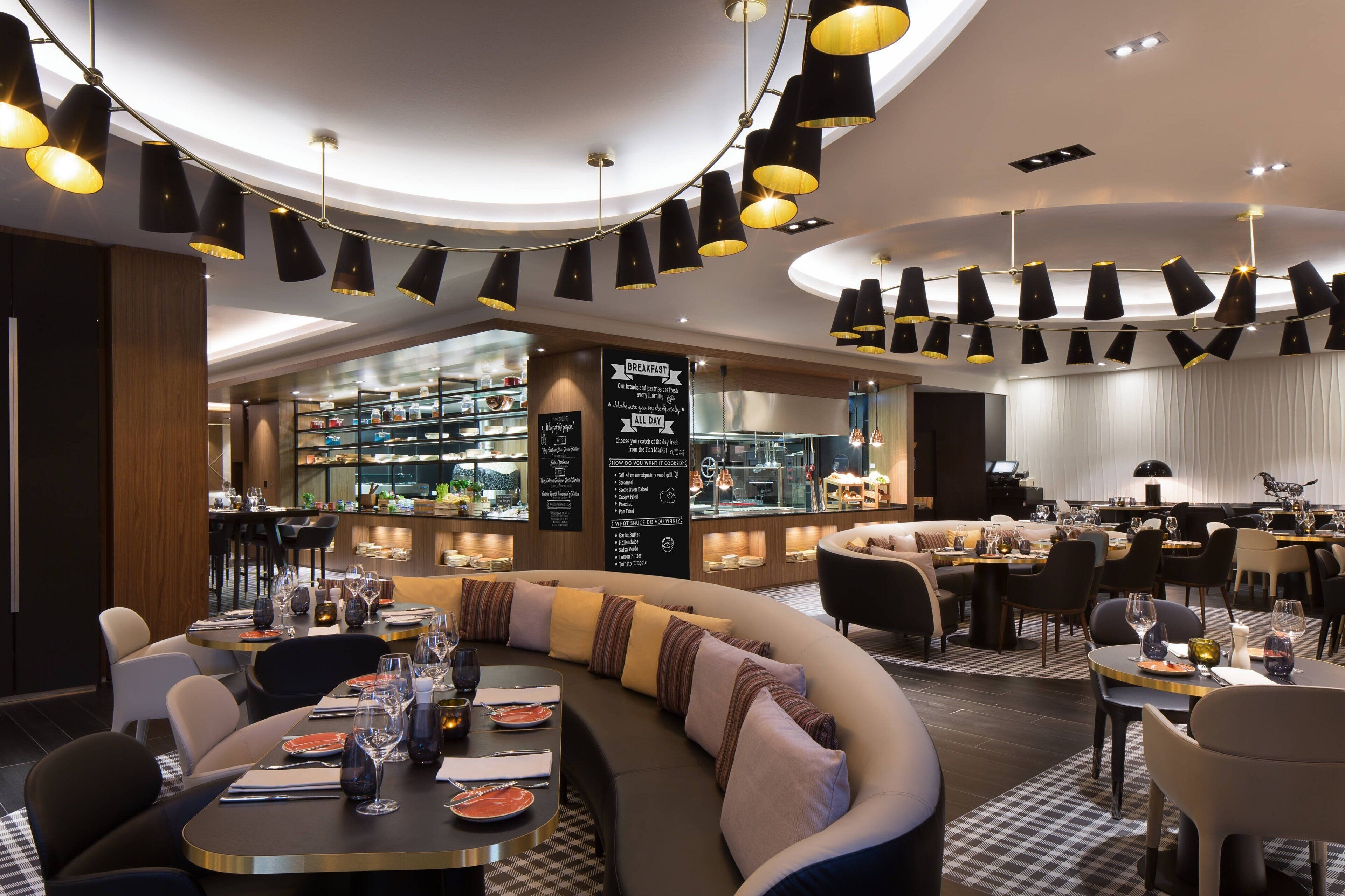 A modern restaurant with a curved seating area, a bar, and a view of the kitchen.