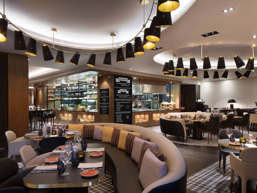 Un restaurant moderne doté d’un espace salon aux lignes courbes, d’un bar et offrant une vue sur la cuisine.