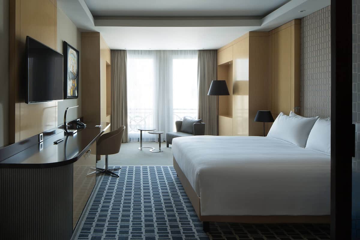 Une chambre d’hôtel avec un lit, un bureau, une chaise, une télévision et une fenêtre avec des rideaux.