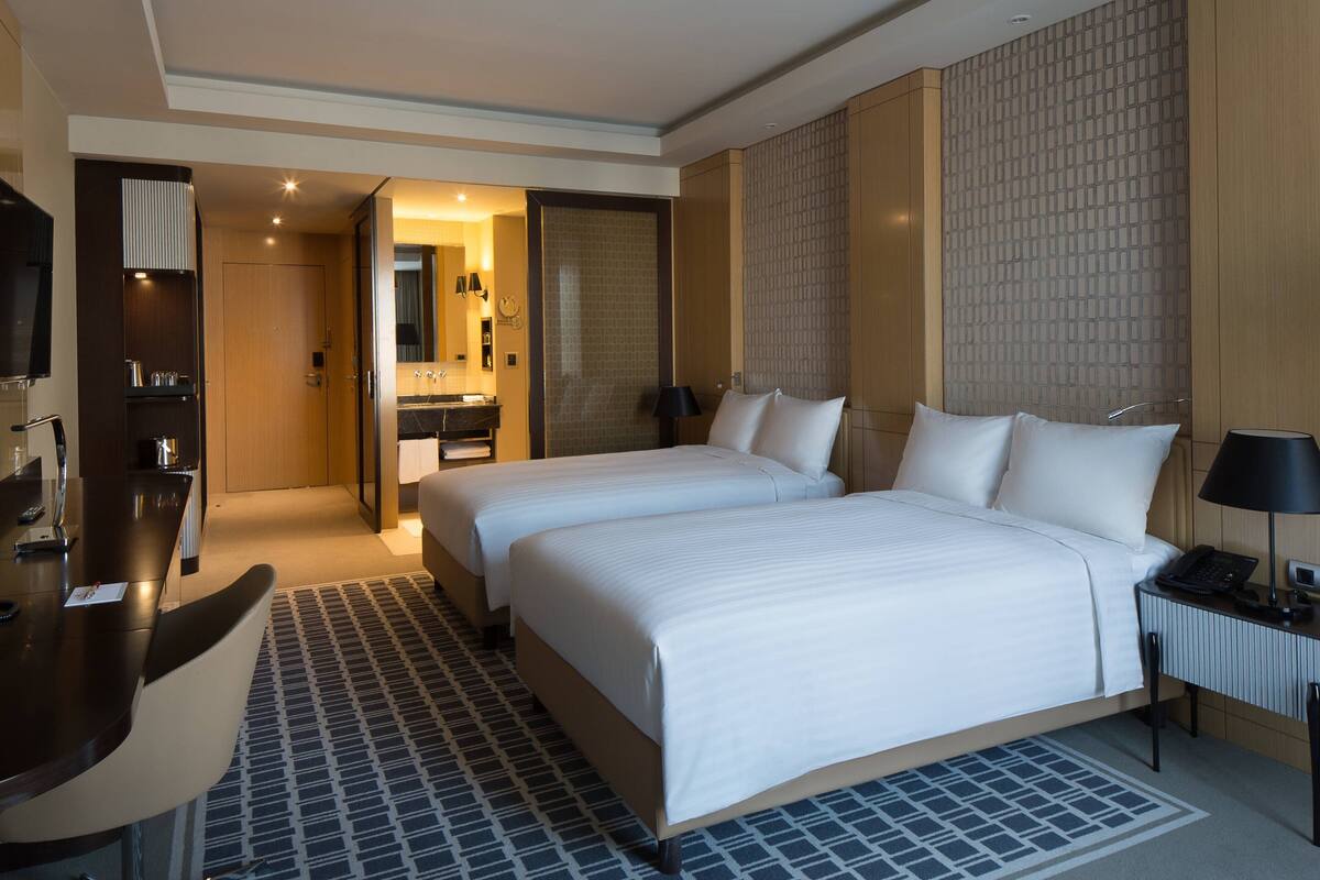 Une chambre d’hôtel avec deux lits, un bureau, une chaise, une salle de bain et un téléviseur.