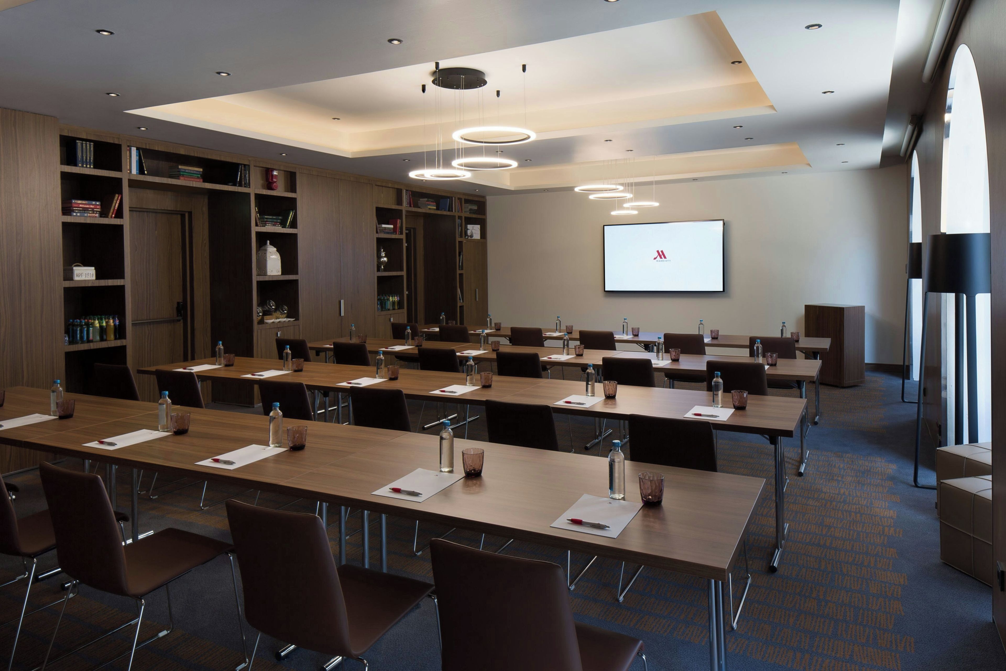 A conference room with multiple tables, chairs, a projector screen, and a bookshelf.