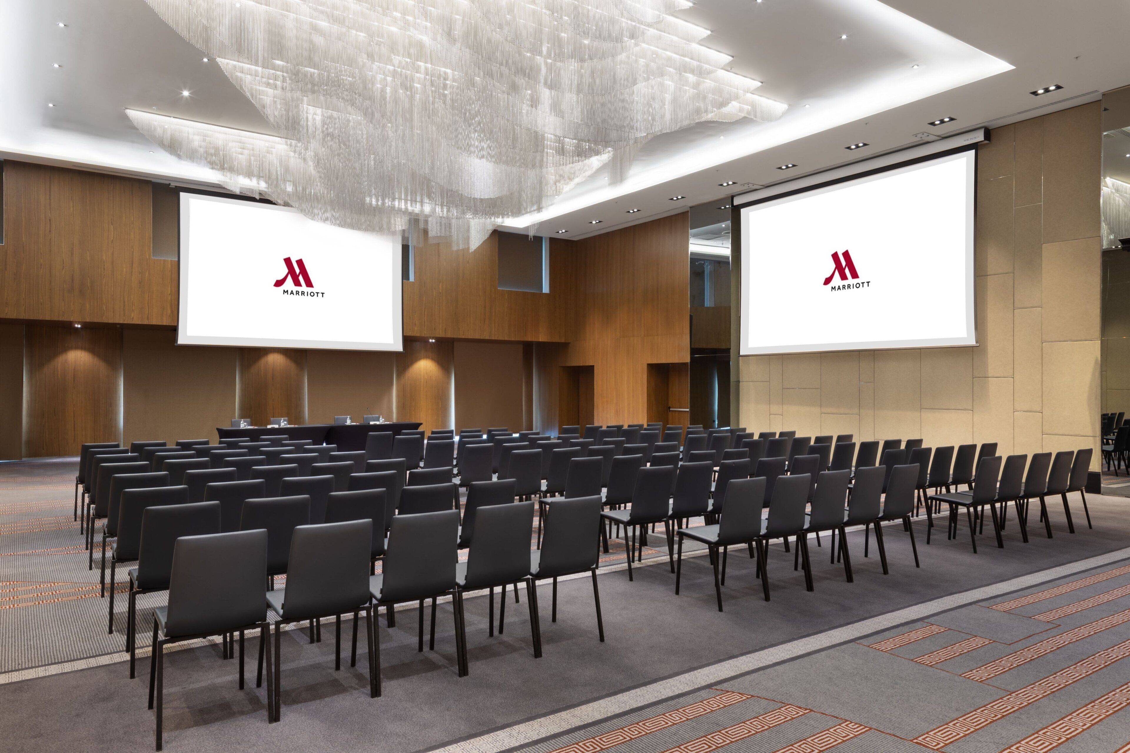 A conference room with rows of chairs, a large screen, and a modern chandelier.