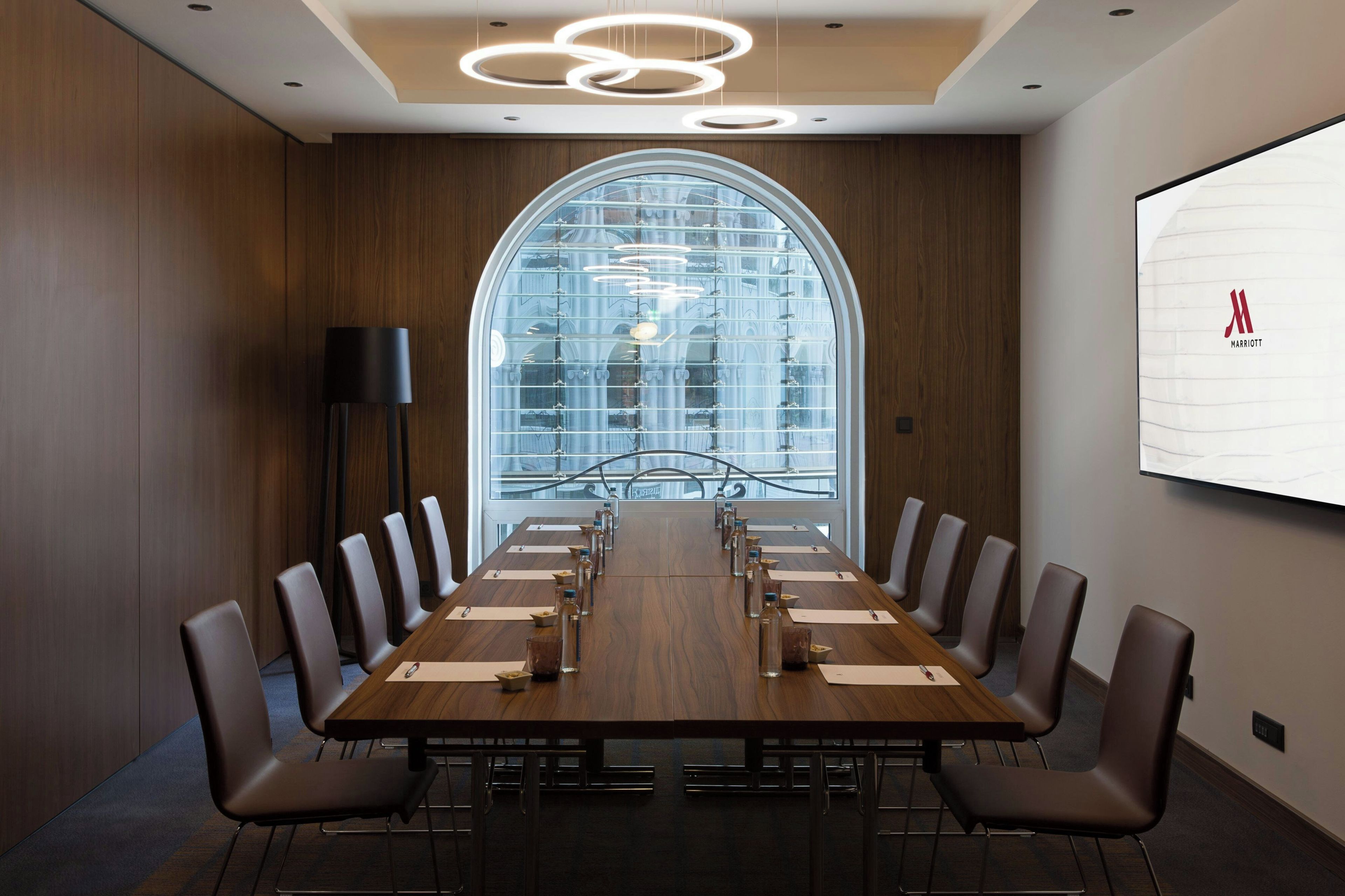 A conference room with a long table, chairs, a projector screen, and a large arched window.