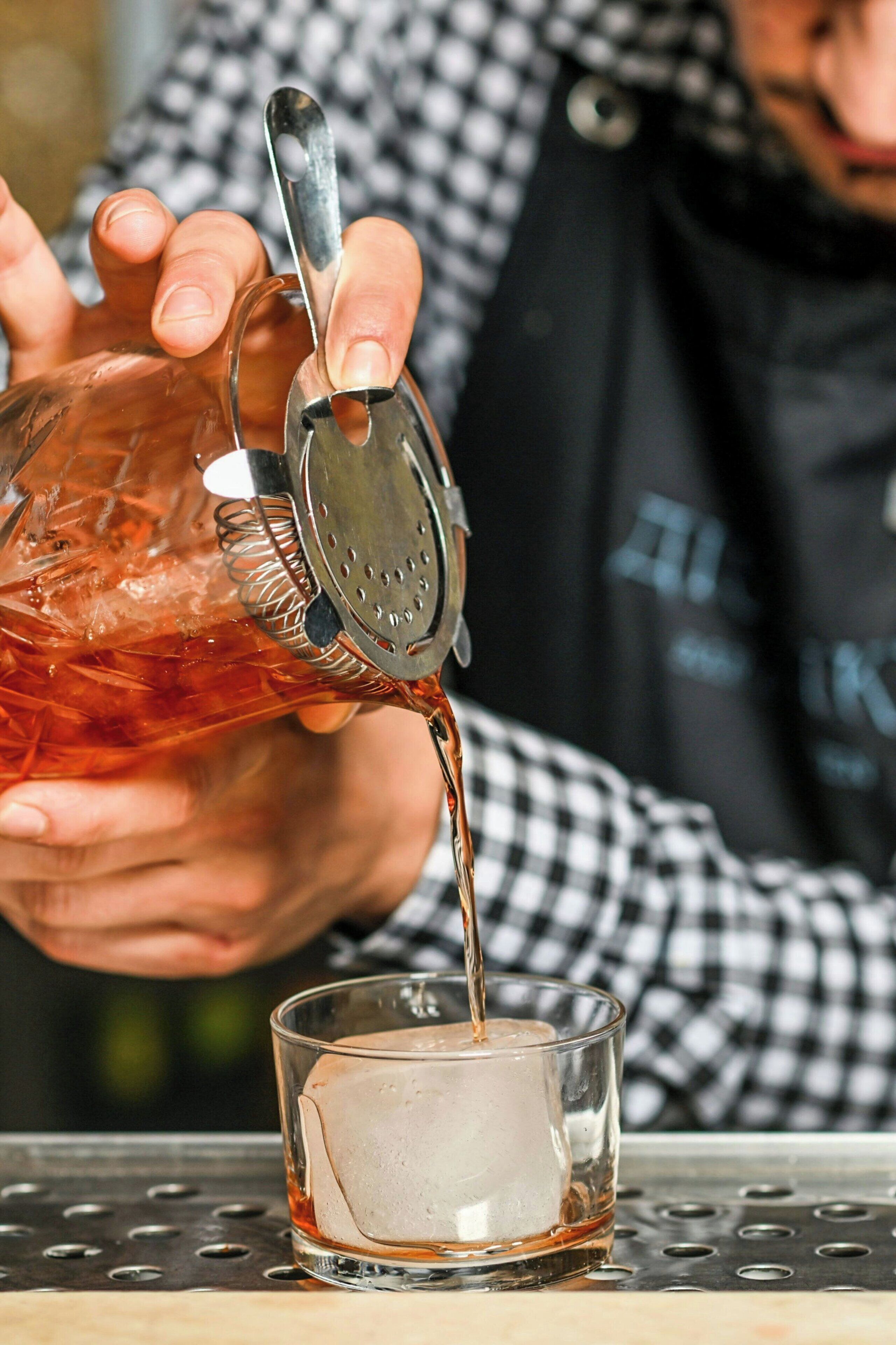 Eine Person gießt Flüssigkeit aus einer Karaffe in ein Glas mit Eis.