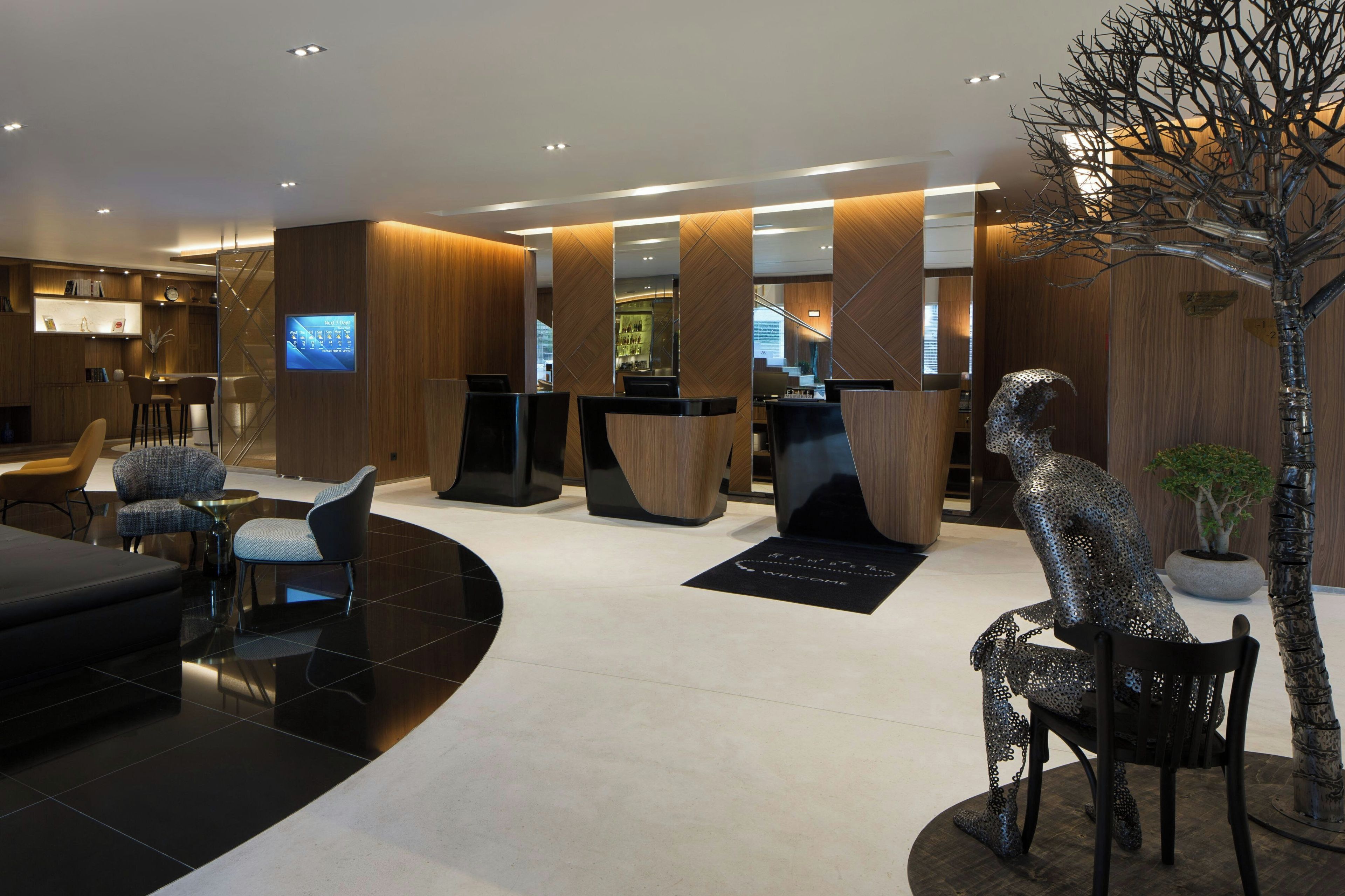 A modern hotel lobby with a reception desk, seating area, and a decorative metal sculpture.