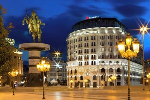 Un edificio histórico con arquitectura clásica, una estatua y el cartel de un hotel Marriott.