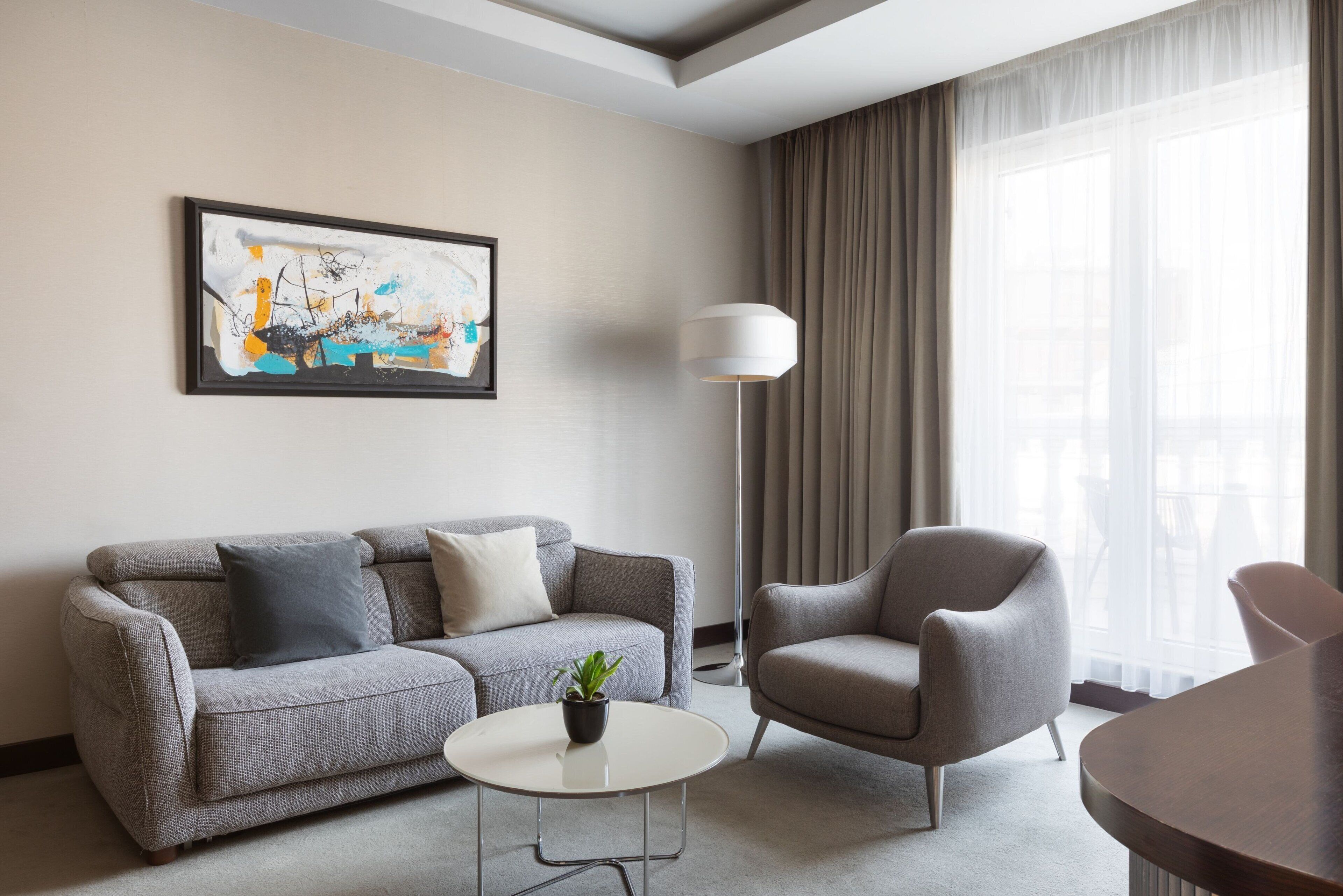 Una sala de estar moderna con un sofá gris, una mesa redonda de centro con una planta, un sillón gris y un cuadro abstracto grande en la pared.