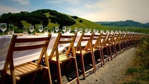 Varias mesas dispuestas al aire libre con sillas, cada una con mantel blanco y copas de vino.