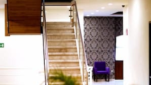 Vestíbulo de hotel con una escalera, un mostrador de recepción y asientos morados.