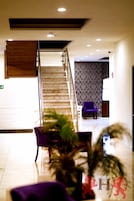 Vestíbulo de hotel con una escalera, un mostrador de recepción y asientos morados.