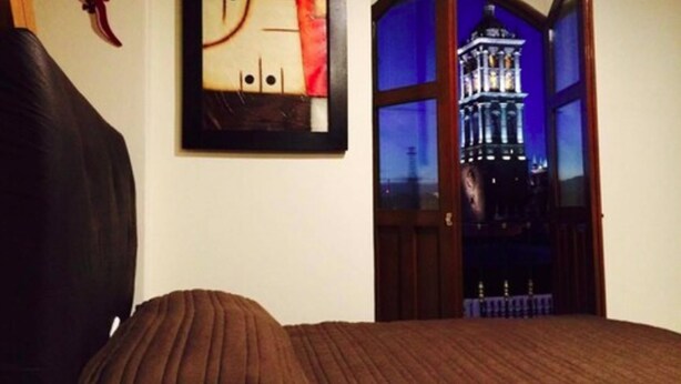 Un dormitorio con cama, un cuadro abstracto colgado en la pared y vistas de un edificio a través de una puerta abierta.
