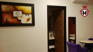 Una habitación de hotel con un cuadro, una puerta que da a un baño y una mesa con sillas moradas.